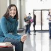 Asain American student sitting on bench with books in hall between classes